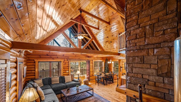 Ein Blockhaushaus-Interieur mit Holzbalkendecke, einem Essbereich und einem gemütlichen Wohnzimmer mit Sofa und Couchtisch.