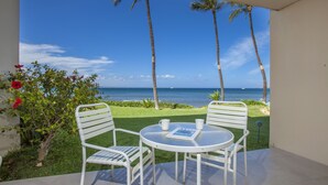 Un patio con un tavolo rotondo e due sedie, con vista su una spiaggia con palme e cielo sereno.