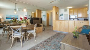 Un'ampia zona giorno con tavolo e sedie da pranzo, TV e cucina dotata di mobili e elettrodomestici in legno.