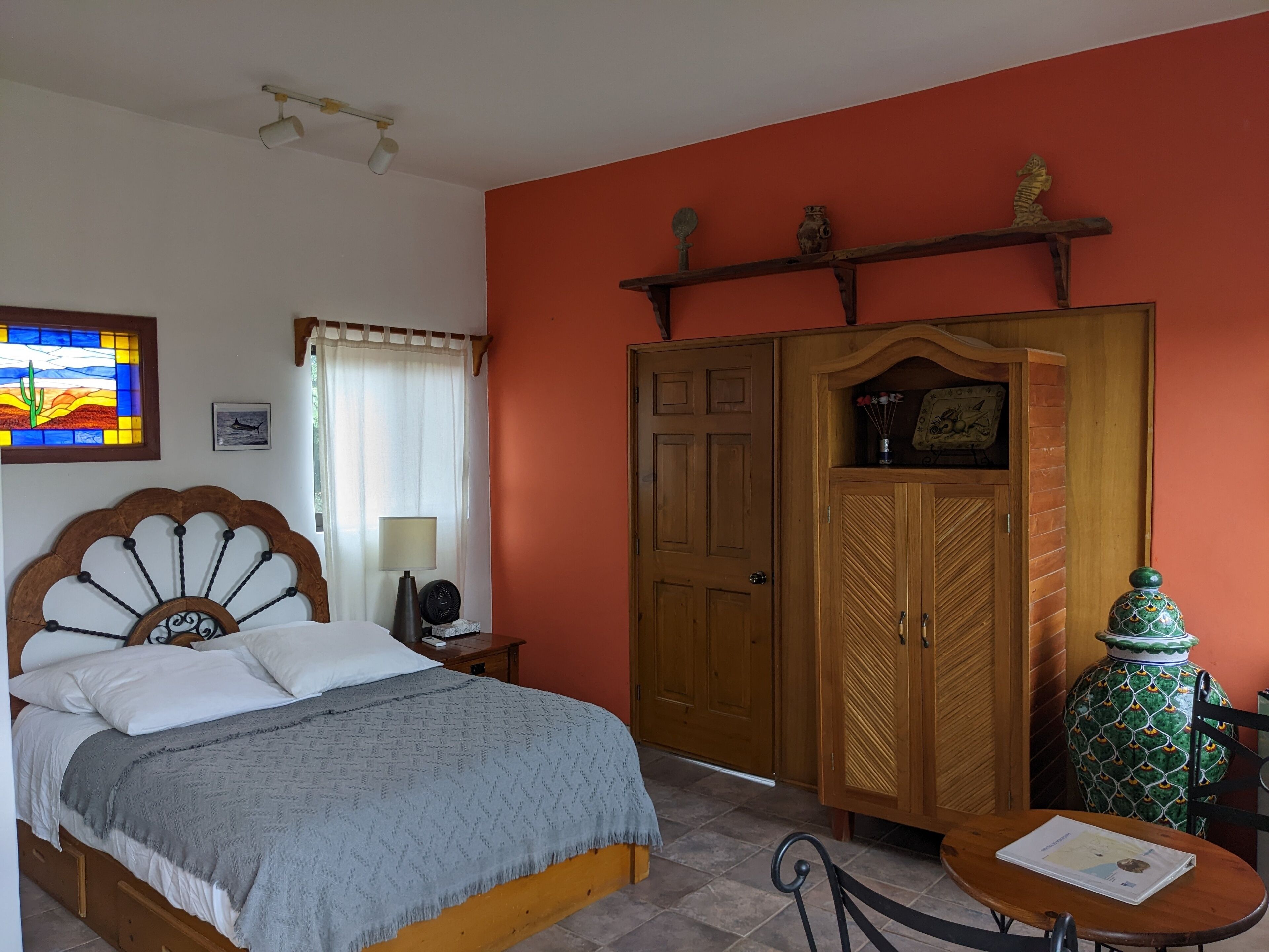 A bedroom with a bed, a wooden wardrobe, a small table, and a decorative vase.