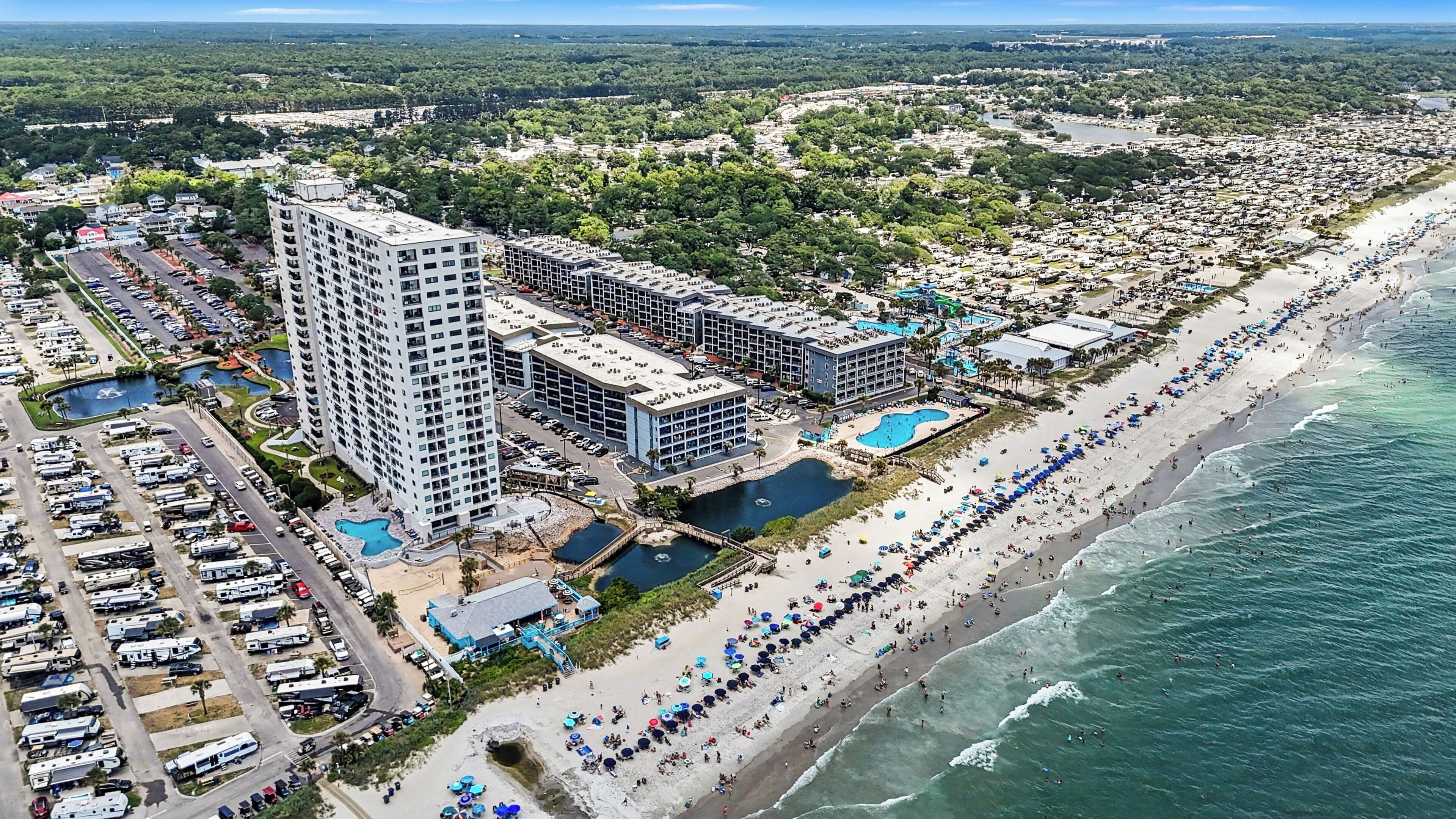 A coastal resort with multiple high-rise buildings, a beach, and a parking lot filled with RVs.