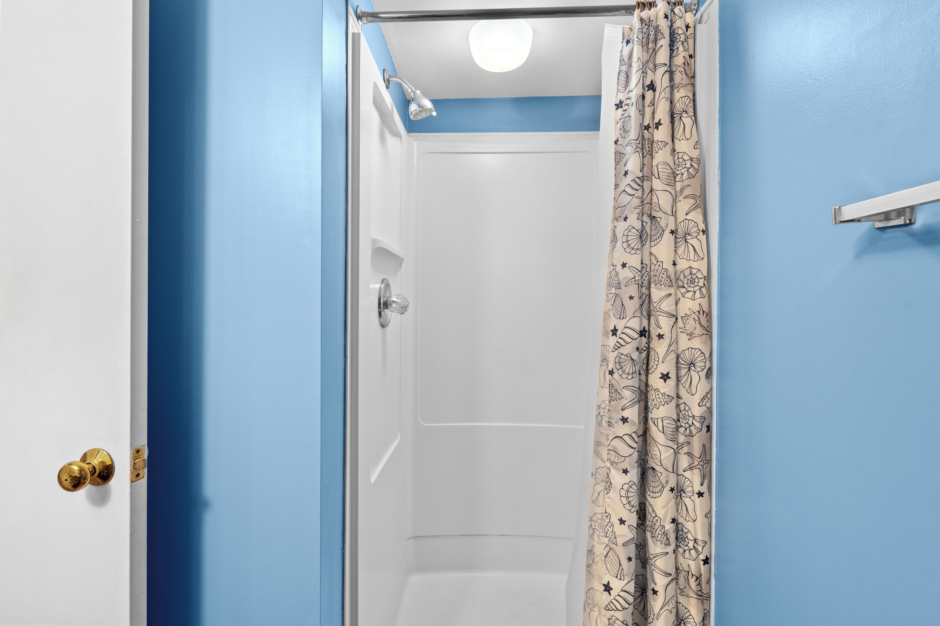 Un baño con ducha, una puerta blanca y una pared azul.