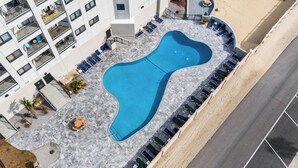 Vista aérea de un hotel con piscina, sillas de descanso y un área ajardinada con palmeras.