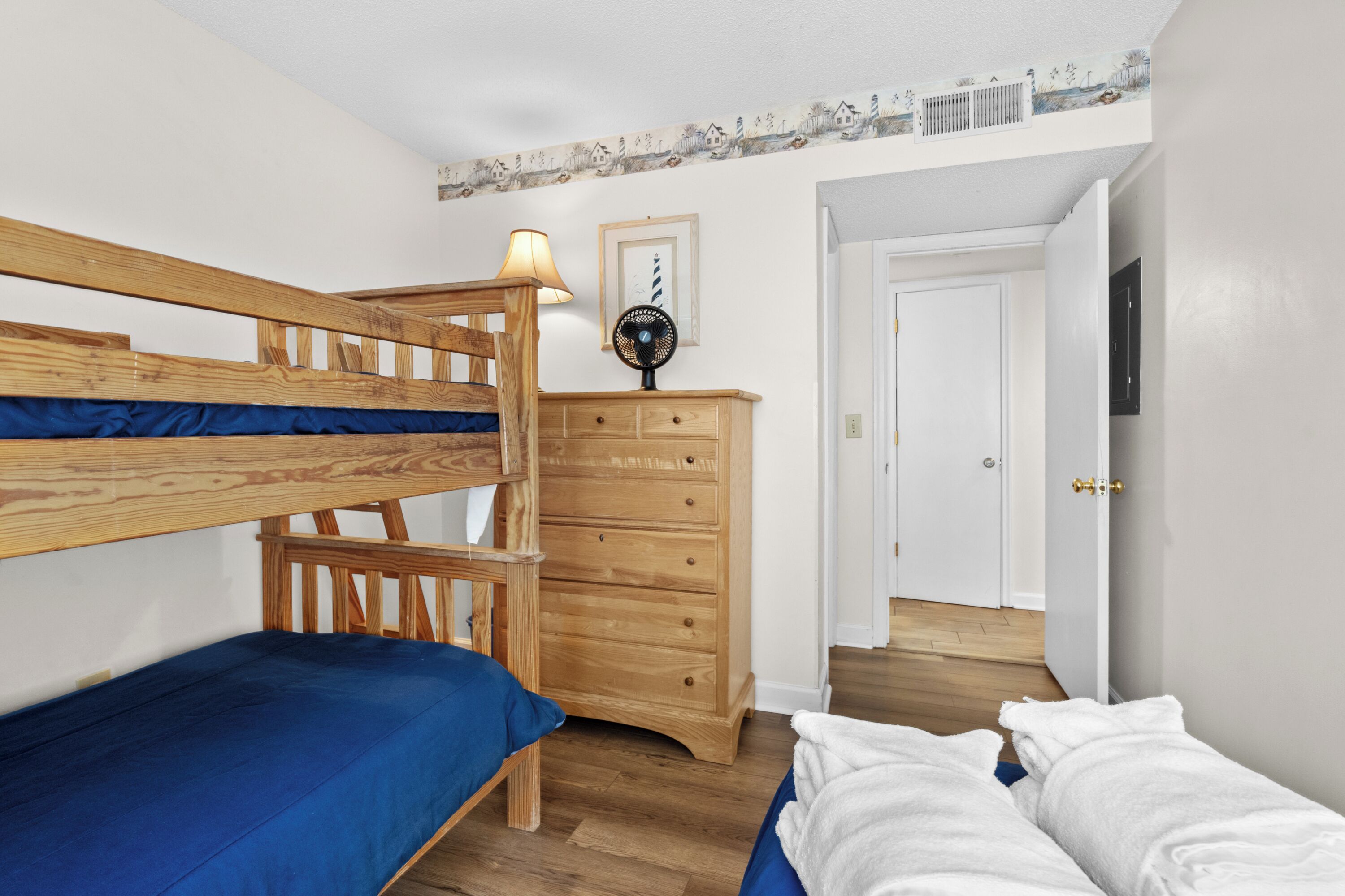 Een slaapkamer met een stapelbed, een houten dressoir en een deur naar een andere kamer.