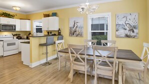 Una cocina moderna con armarios blancos, una isla central y una zona de comedor con sillas de madera.