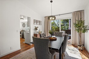Uma sala de jantar com mesa, cadeiras, luminária pendente e vista para o exterior.
