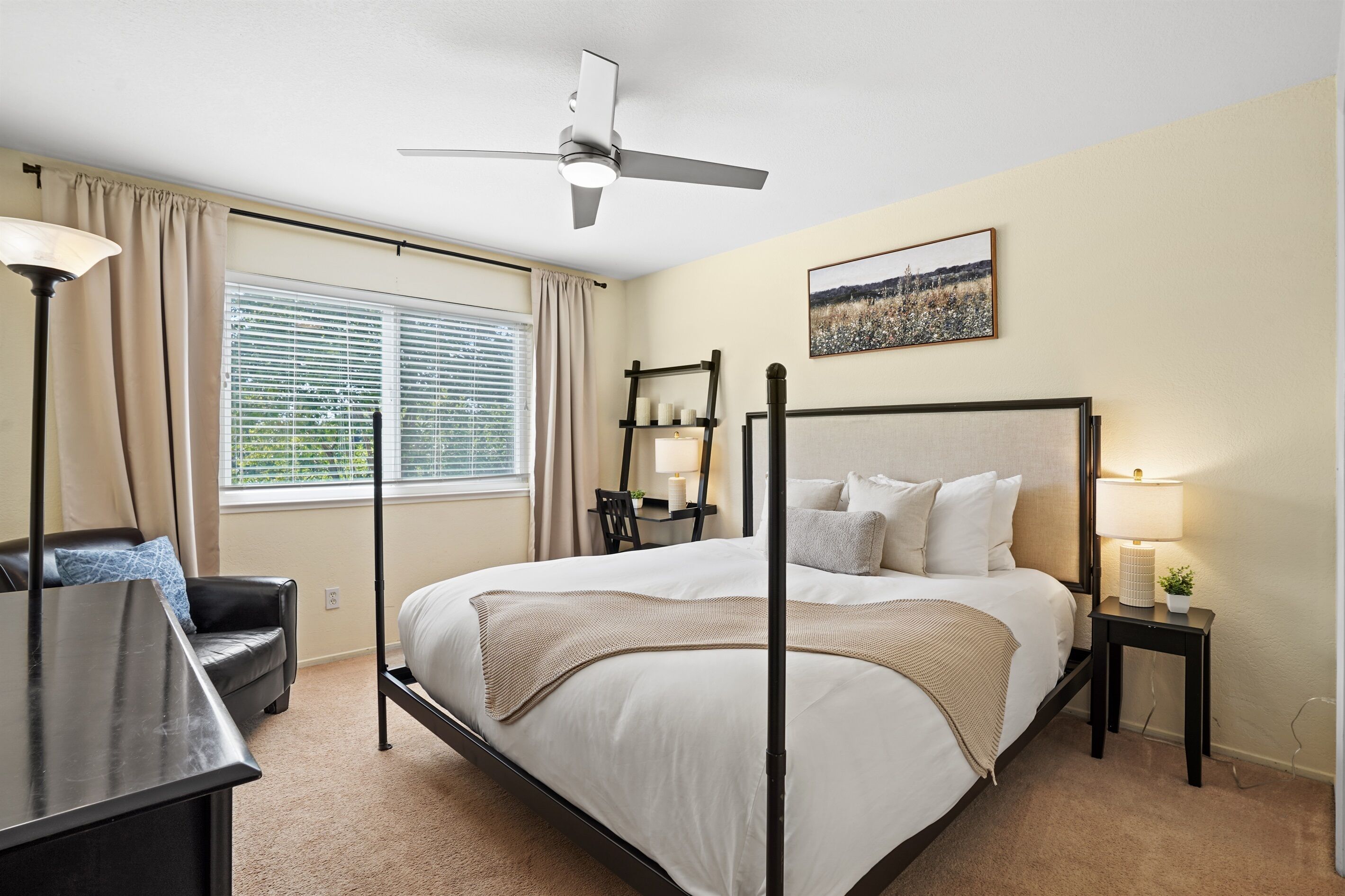 A four-poster bed with a ceiling fan, a desk with a lamp, and a view of the outdoors through the window.