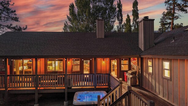 Una cabaña acogedora con jacuzzi, terraza de madera y vistas al bosque circundante.