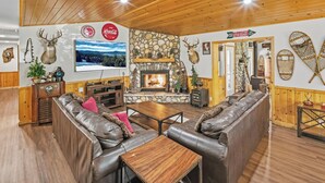 Una sala de estar acogedora con chimenea de piedra, sofás de cuero y un televisor montado en la pared.