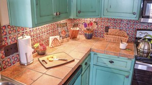 A kitchen with teal cabinets, a tiled backsplash, and a countertop with various kitchen utensils and a cutting board. - Maverick cabin North Rim (Canyon)