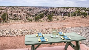 A picnic table with plates, glasses, and a pitcher set against a rocky landscape with a fence and a sign in the background. - Maverick cabin North Rim (Canyon)