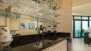 Una cocina con encimera de granito, un lavamanos, una licuadora y una estantería de vidrio con copas de vino.