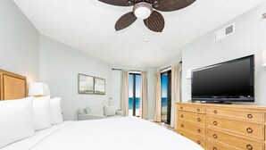 Un dormitorio con cama, televisor, ventilador de techo, cómoda y vista al océano.