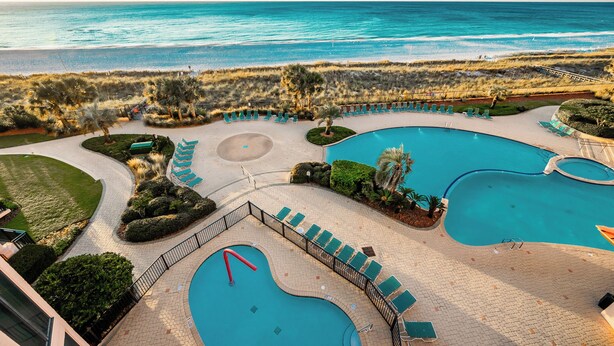 Un resort con múltiples piscinas, vista a la playa y un paisaje bien cuidado.
