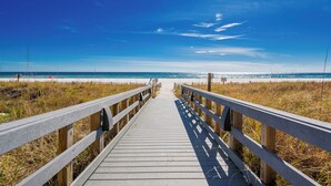 Pasarela de madera que conduce a una playa con cielos despejados y aguas tranquilas.
