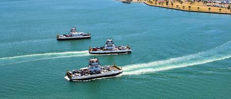 Three large boats on a calm sea with a coastal cityscape in the background.