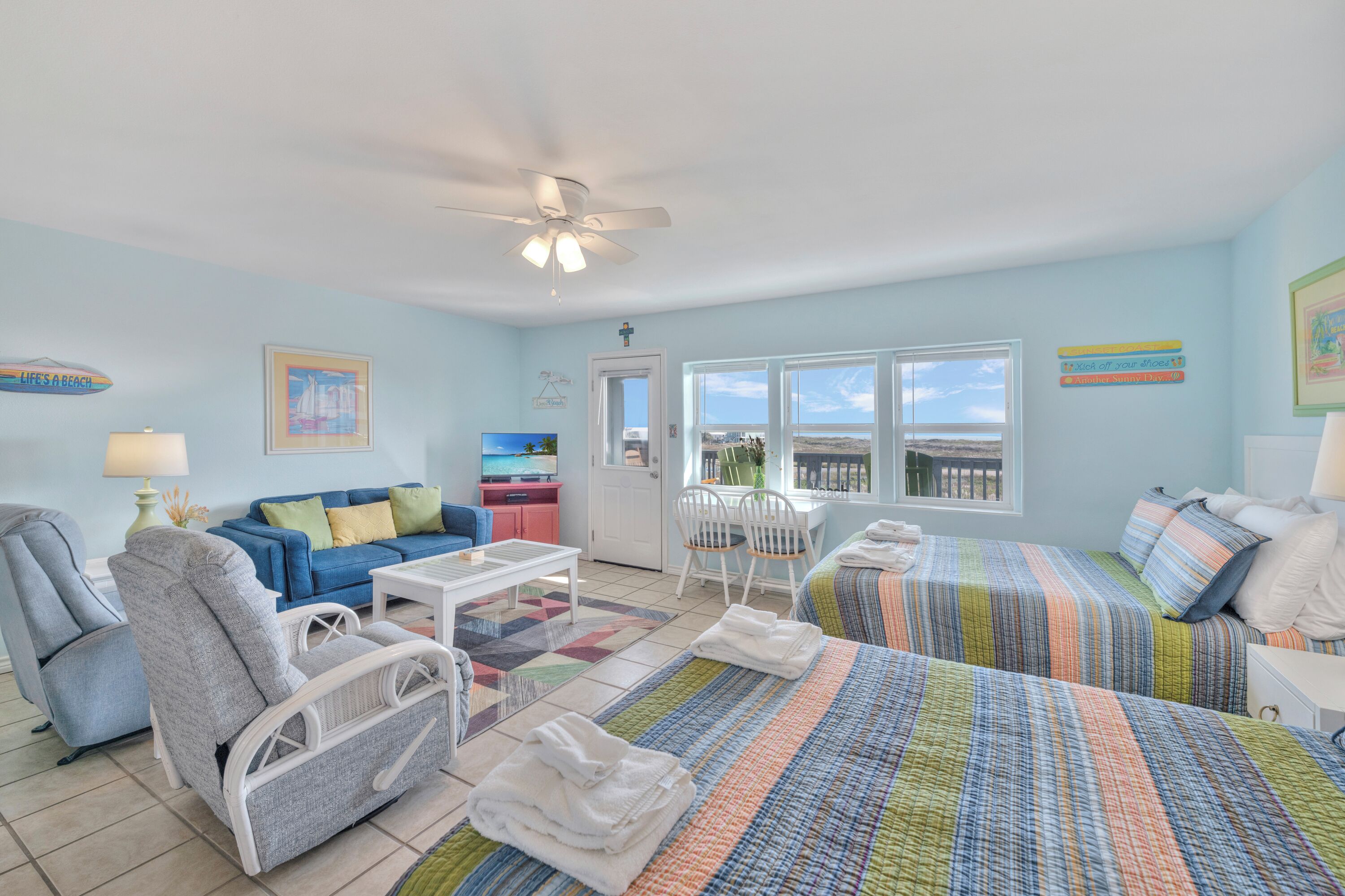A room with a bed, a chair, a sofa, a table, and a ceiling fan.