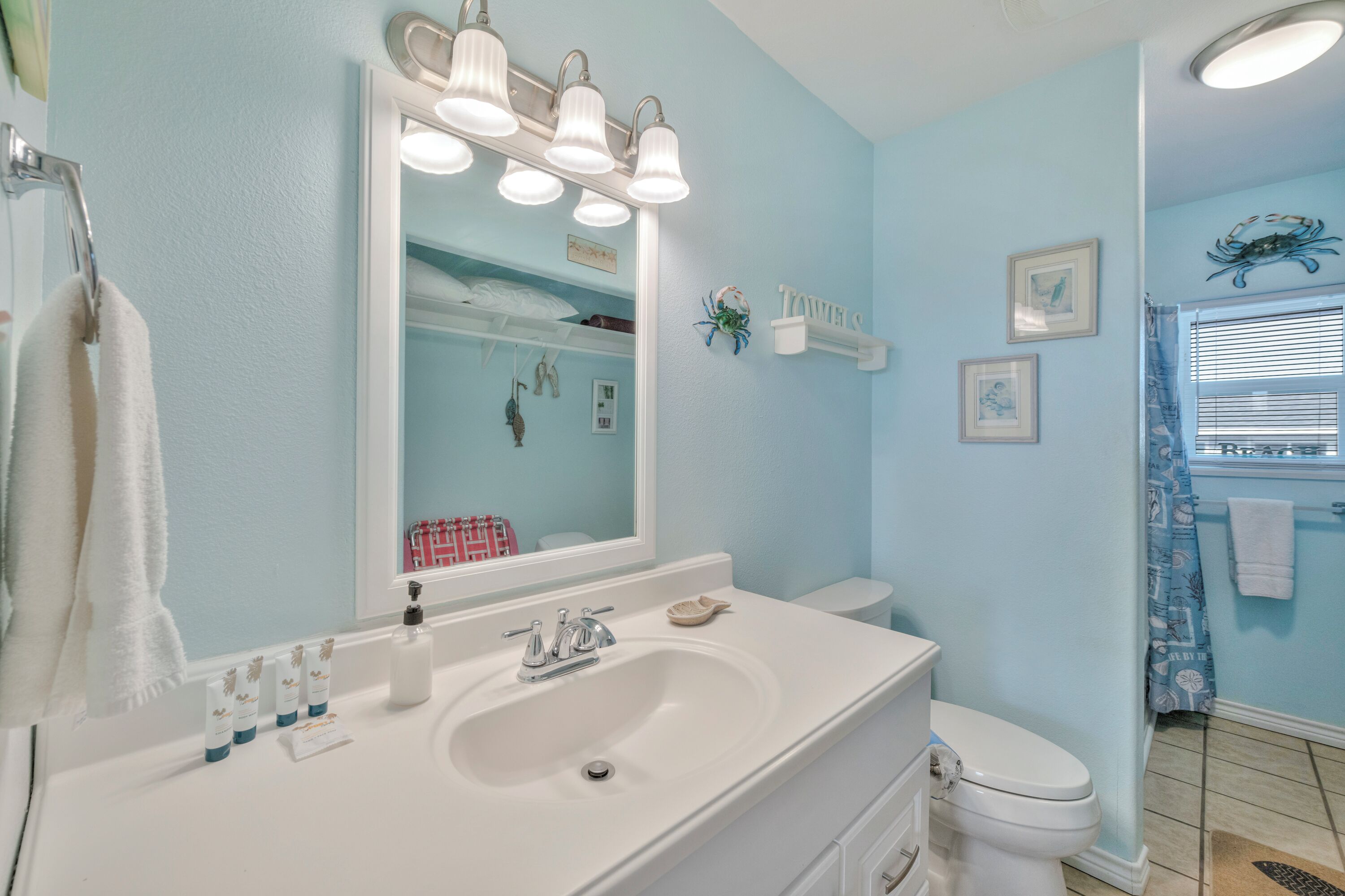Une salle de bain avec un lavabo blanc, un miroir avec éclairage intégré, des toilettes et un rideau de douche.