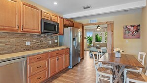 A modern kitchen with wooden cabinets, stainless steel appliances, and a dining area with a wooden table and white chairs.