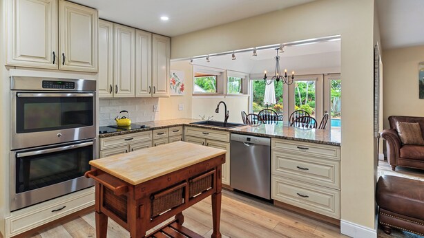 A modern kitchen with stainless steel appliances, a wooden dining table, and a view of the outdoors.