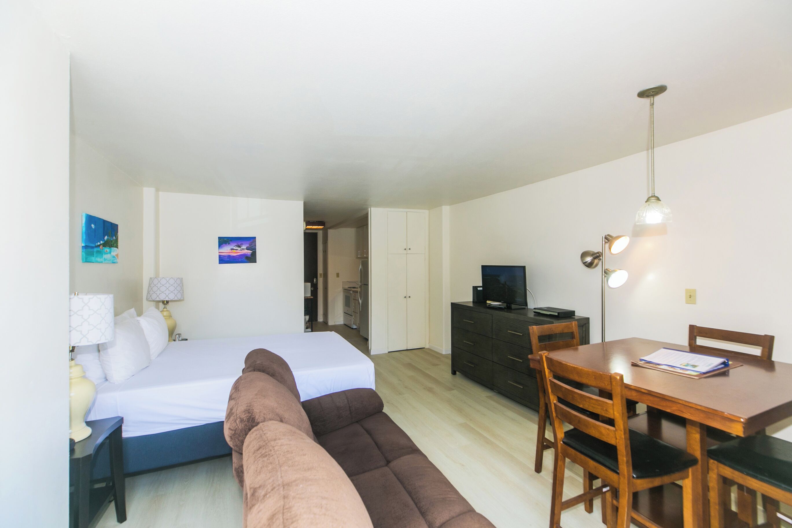 Un dormitorio con cama, sofá, escritorio, cómoda, televisor y mesa de comedor con sillas.
