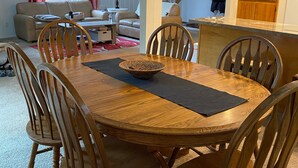 Un comedor con una mesa redonda de madera, seis sillas de madera y un mantel tejido en el centro.