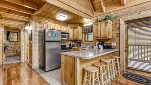 Interior de una cabaña de madera con cocina, que incluye un refrigerador, microondas y taburetes de bar.