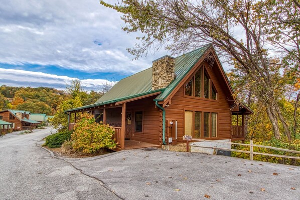 A rustic lodge with a stone chimney, wooden exterior, and a porch with a railing.
