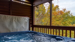 Un jacuzzi en una cabaña de madera con vista a árboles otoñales.