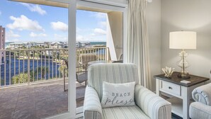 Un balcone con vista su un porto turistico e degli edifici, una poltrona a righe con un cuscino, un comodino con una lampada e una finestra con tende.