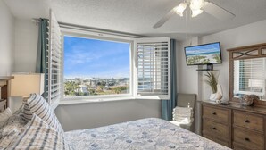 Una camera da letto con un letto, una TV, una cassettiera e una finestra con vista su edifici e alberi.