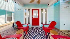 A covered porch with a red door, red chairs, and a patterned rug. - Townhome Located in Town, Close to beach, Shared Pool, Pet Friendly (Port Aransas)