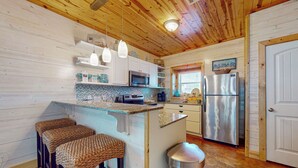 A kitchen with wooden ceiling, white cabinets, stainless steel appliances, and a small island with stools. - Townhome Located in Town, Close to beach, Shared Pool, Pet Friendly (Port Aransas)