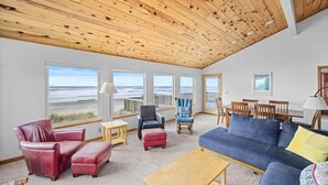 A spacious living room with a wooden ceiling, large windows with ocean views, a blue sofa, and a red leather chair. - la Playa Luna-Family sized beachfront home (Cloverdale)