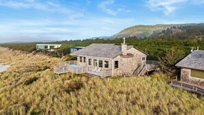 A stone house with a deck and a large window, surrounded by tall grass and hills. - la Playa Luna-Family sized beachfront home (Cloverdale)