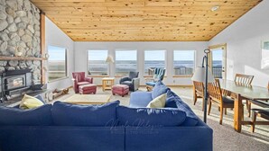 A cozy living room with a stone fireplace, wooden ceiling, and large windows offering ocean views. - la Playa Luna-Family sized beachfront home (Cloverdale)