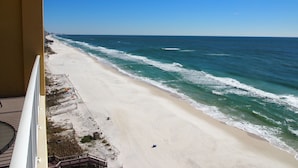 Une vue sur la plage depuis un balcon, avec un ciel dégagé, une plage de sable et les vagues de l’océan.