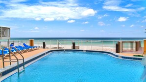 Une piscine avec vue sur l’océan, entourée de chaises longues bleues et d’une clôture blanche.