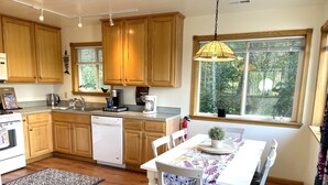 A kitchen with wooden cabinets, a dishwasher, a coffee maker, and a dining table with chairs. - Family vacation destination! Lake activities and game house! (Kenai)
