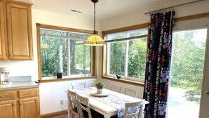 A kitchen with wooden cabinets, a dining table with chairs, a coffee maker, and large windows with curtains. - Family vacation destination! Lake activities and game house! (Kenai)