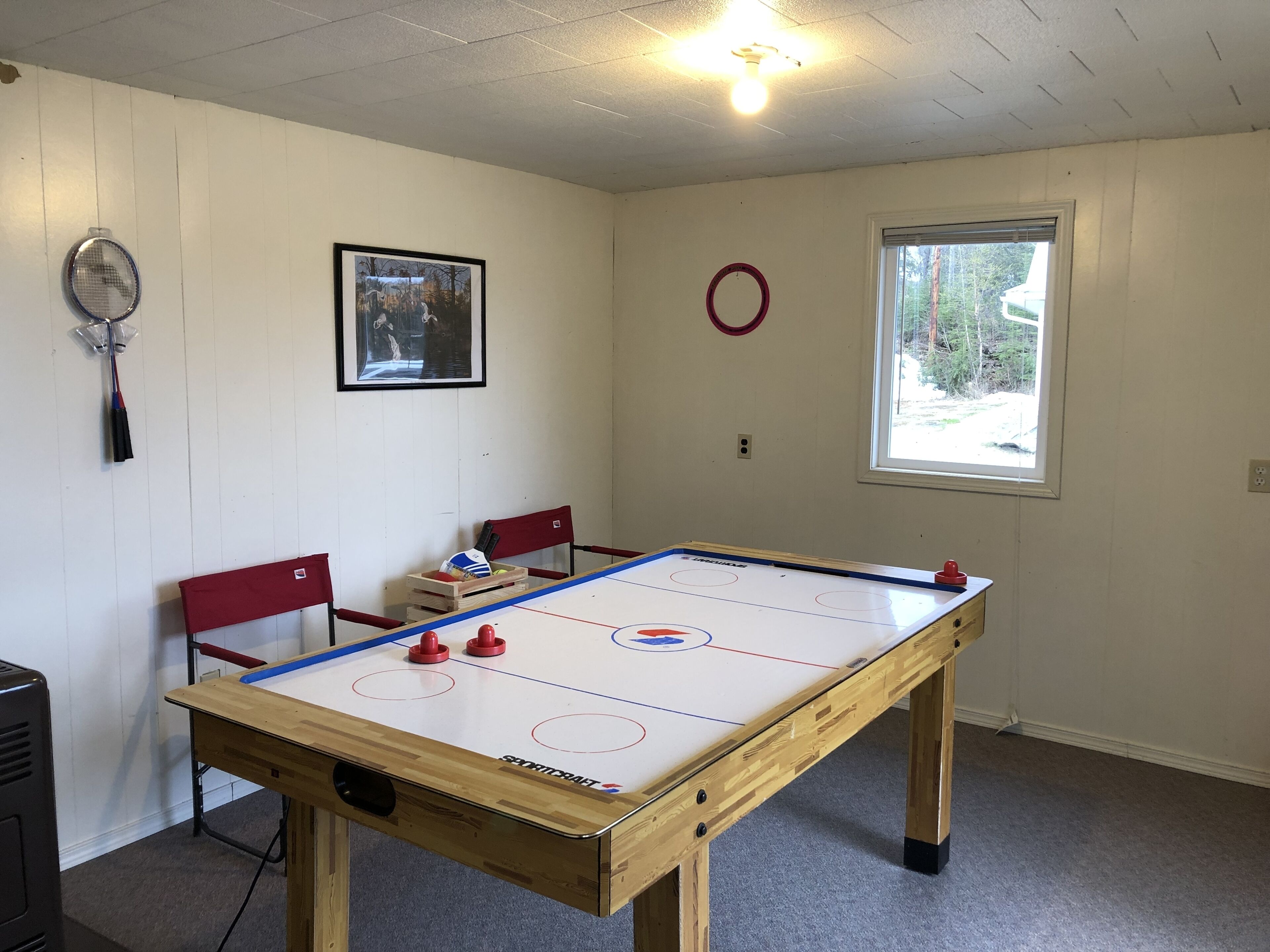 Una habitació amb taula de futbolí, taula de ping-pong i finestra amb vista a arbres.