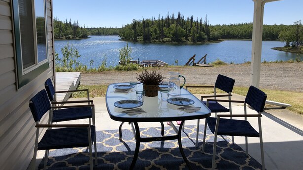 A covered patio with a table set for four, overlooking a lake and forest. - Family vacation destination! Lake activities and game house! (Kenai)