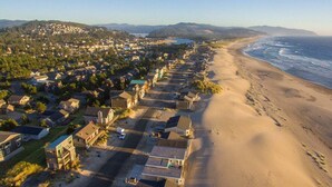 Vista aerea di una zona residenziale costiera con case lungo una spiaggia sabbiosa, un cielo sereno e colline in lontananza.