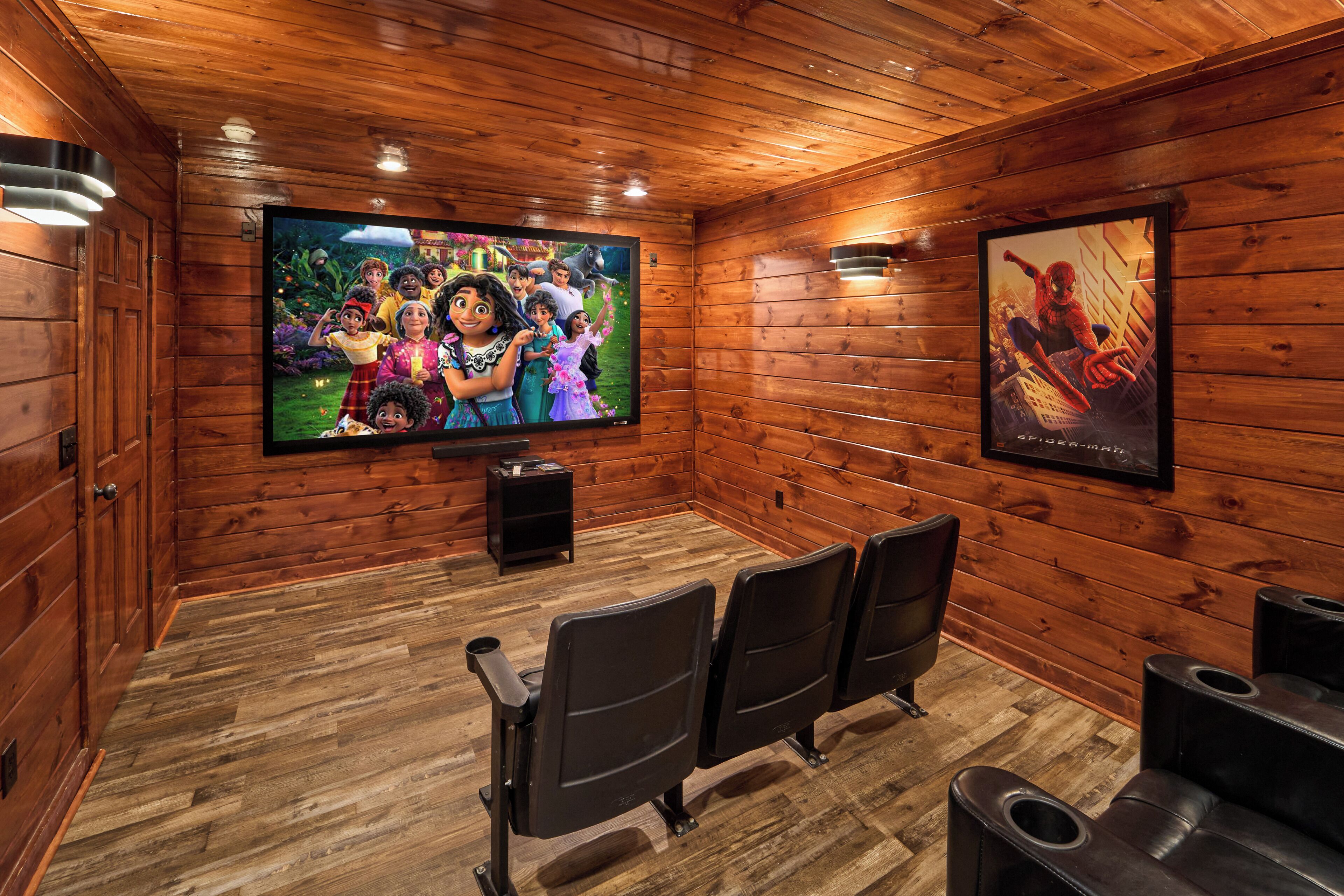 Una habitación con paneles de madera, un televisor de pantalla plana grande, sillas negras y un cartel en la pared.