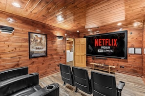 Un intérieur en bois avec un grand téléviseur à écran plat affichant « NETFLIX PREMIUM 4K ULTRAHD » et une affiche du film « Le Seigneur des anneaux ».