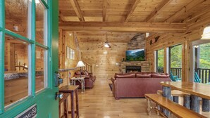 Interior de una cabaña de madera con chimenea, asientos de cuero y comedor.