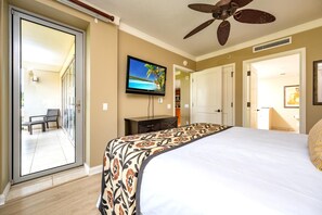 A hotel room with a large bed, a flat-screen TV mounted on the wall, a ceiling fan, and a sliding glass door leading to an outdoor area with a chair.