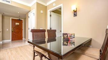 A hotel room with a glass dining table, two brown chairs, a wall-mounted light, and a poster on the wall.