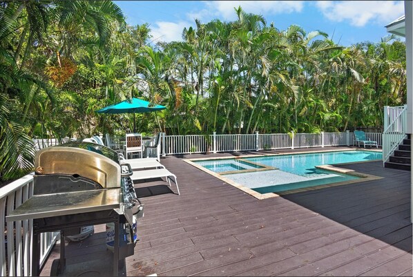 A pool area with a barbecue grill, lounge chairs, and a white fence.