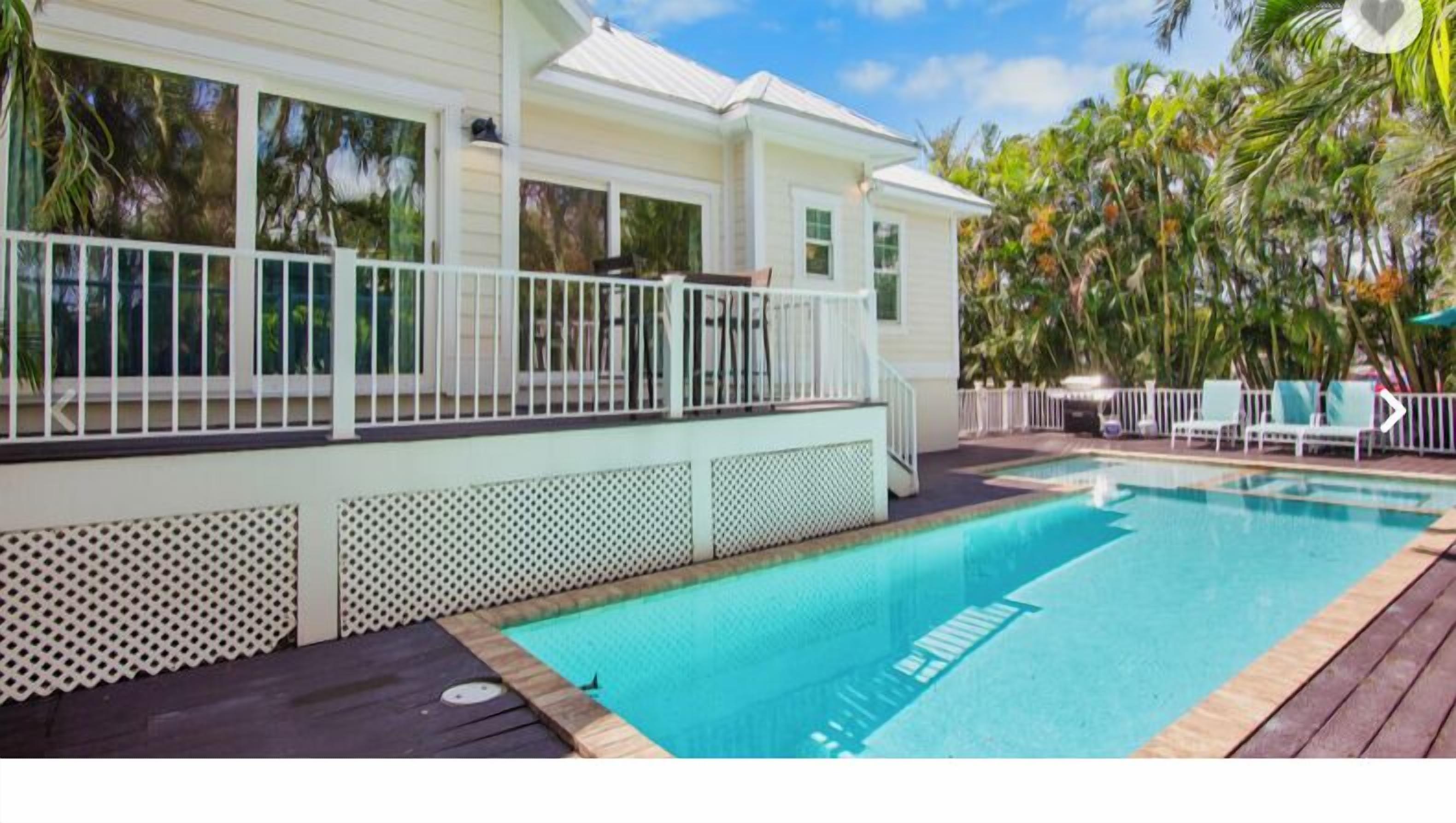 A pool area with a wooden deck, a white fence, and a house with large windows.